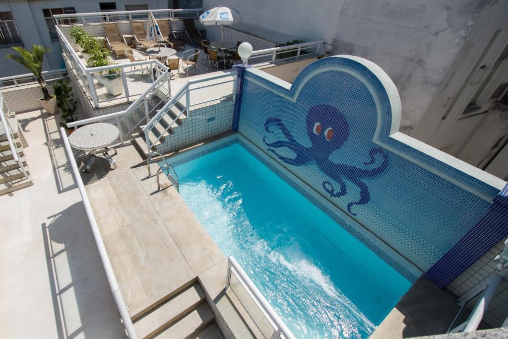 Hóspedes desfrutando da ampla e convidativa piscina do Hotel OK, um espaço perfeito para relaxamento e lazer sob o céu azul.